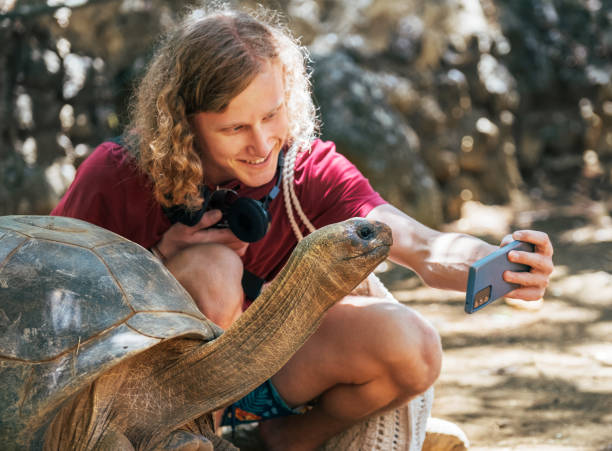 istock Smiling tourist boy making a selfie using cell phone with Aldabra giant tortoise endemic species - one of the largest tortoises in the world in the zoo nature park on Mauritius island. 2152754464