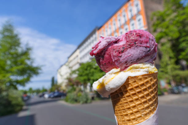 A close-up of a vibrant ice cream cone against a blurred Berlin street backdrop. The sunny day enhances the cheerful, urban vibe.
