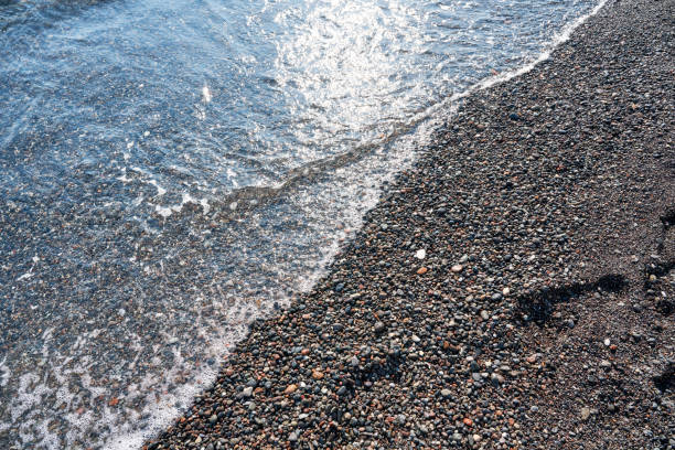 Detail of cobblestones in the transparent water of the famous Vlychada Beach, Santorini. Background, natural stone, texture.