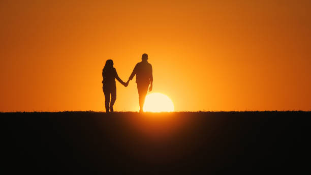 istock A young couple walks across a field towards the setting sun, holding hands 2152759499