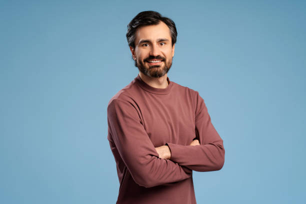 istock Positive bearded young man with arms crossed, looking at camera posing in studio, isolated on blue 2152760594