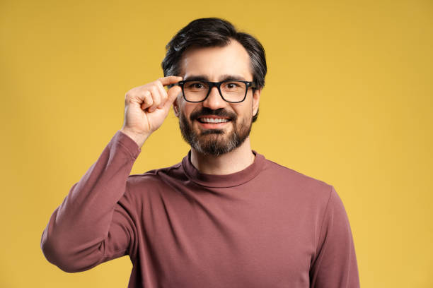 istock Happy young man touching glasses looking at camera in studio, isolated on yellow background 2152760616