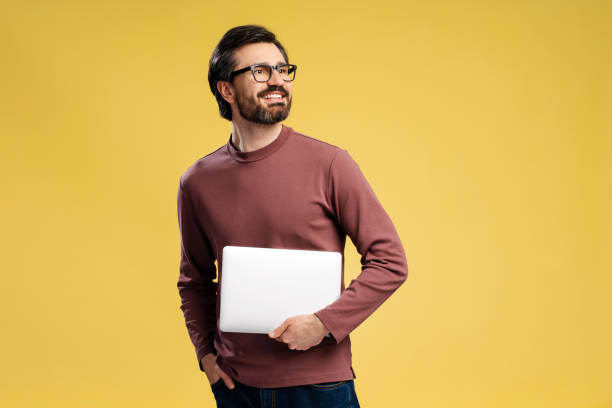 istock Happy young man in eyeglasses with laptop posing in studio, isolated on yellow 2152760620