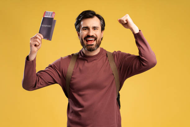 istock Smiling bearded man screaming, holding passport and ticket while holding hands up, isolated 2152760653
