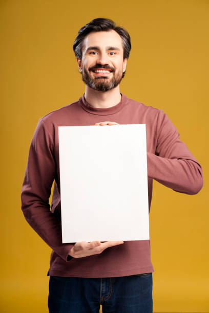 istock Smiling man holding white empty board for advertisement or text, isolated on yellow 2152760673