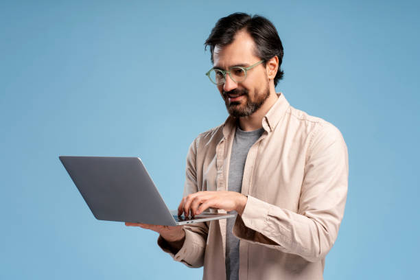 istock Young man in glasses using laptop, typing, isolated on blue background. Online technology 2152761770