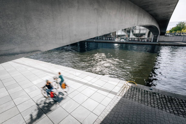 Dynamic shot of three cyclists in motion, riding under a concrete bridge over a canal in Berlin. This urban scene captures the essence of city life and modern architecture.