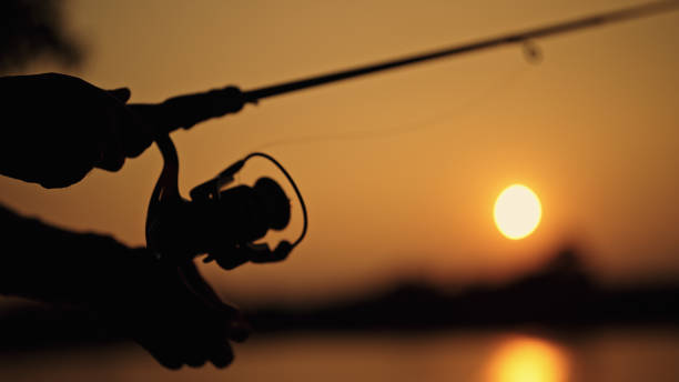Silhouette of man fishing at lake during sunset.