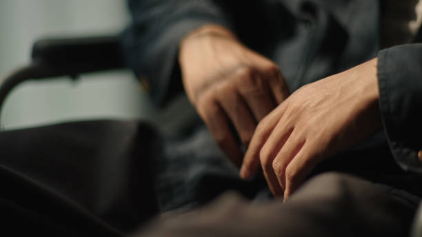 Close-up hand of patient man while sitting on wheelchair.
