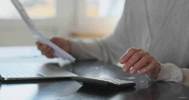 istock Elderly Woman's hands hold bills for services and calculate cost figures on calculator. Close-up, side view. Concept of financial literacy 2152774506
