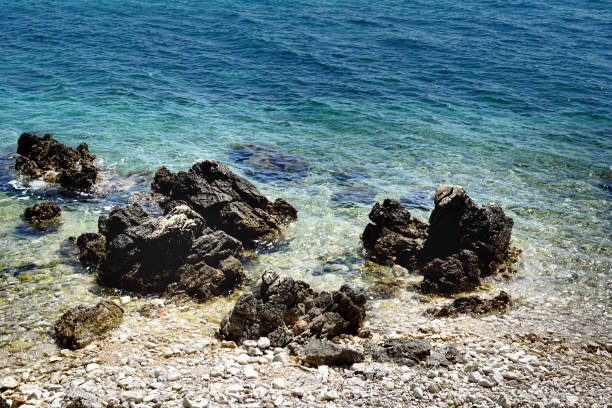 Pebble beach with sharp black rocks in the shallow sea in pristine nature