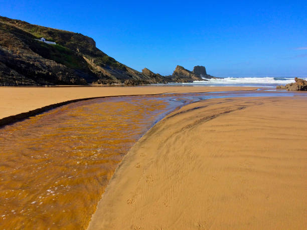istock A sandy beach with a stream, surrounded by rocky cliffs under a clear blue sky. 2152785570
