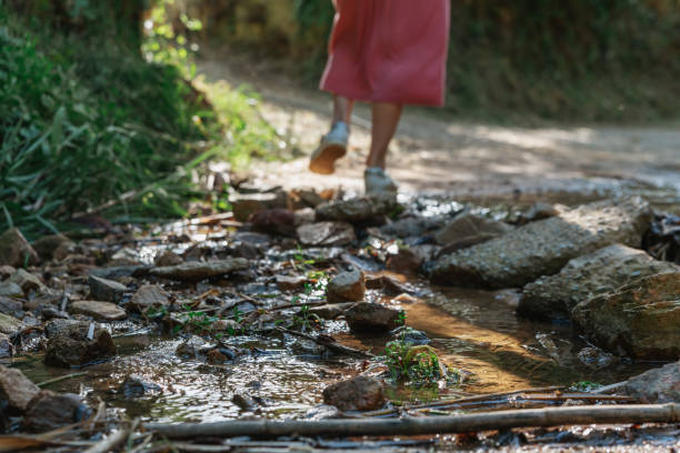 A girl crosses a small stream in a dress in summer, only her legs are visible.