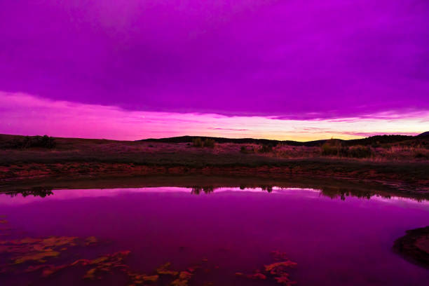 Intense Aurora Borealis Northern Lights - The Northern Lights geomagnetic storm reflected in small pond at night with intense colors in sky including, pinks, purples, blues, greens, and magentas. Geomagnetic storm light phenomenon. in upper levels of Earth's atmosphere.