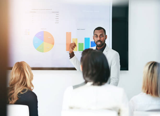 istock Black man, coaching and chart with screen for presentation, meeting or corporate statistics at seminar. Businessman, manager or speaker talking to employees on company revenue, growth or profit 2152803613