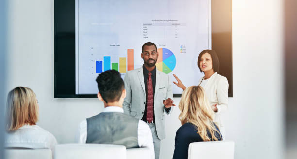 istock Business people, coaching and chart with screen in presentation, meeting or corporate statistics at seminar. Businessman, manager and speaker talking to employees on company revenue, growth or profit 2152803614