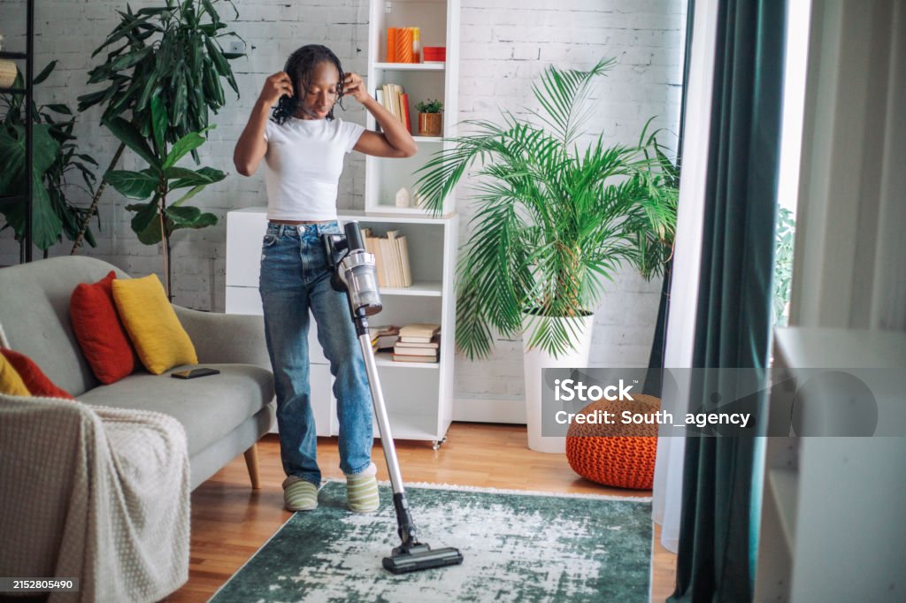 Vacuuming living room with stylish design elements The person vacuums their living space, which is adorned with plants and a mix of modern and traditional decor elements Generation Z Stock Photo Vacuuming living room with stylish design elements The person vacuums their living space, which is adorned with plants and a mix of modern and traditional decor elements Generation Z Stock Photo