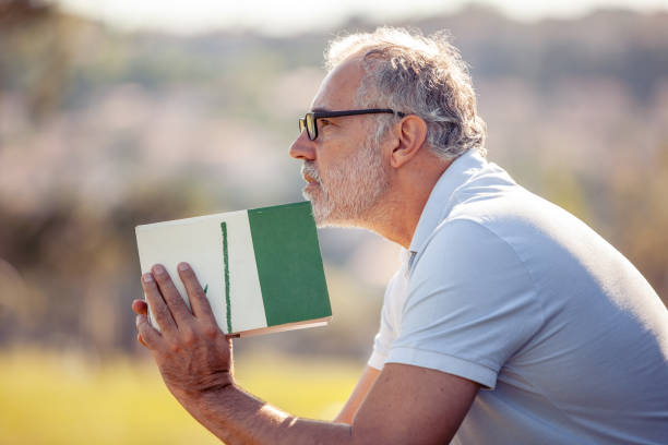 Middle-aged man portrait daydreaming while reading a book in the public park