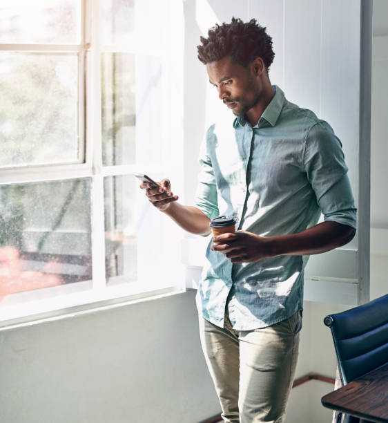 istock Office, window and black man with phone, coffee and scroll on social media, email or online chat. Networking, schedule and creative professional with smartphone for business connection with drink. 2152821941