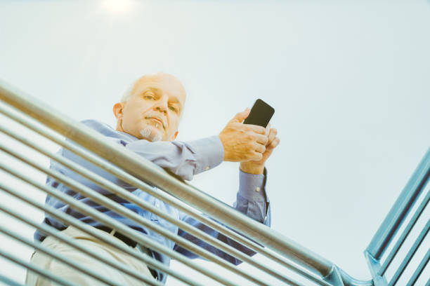 Outdoor setting captures a man intensely using his smartphone, supported by a metal railing in sunlight