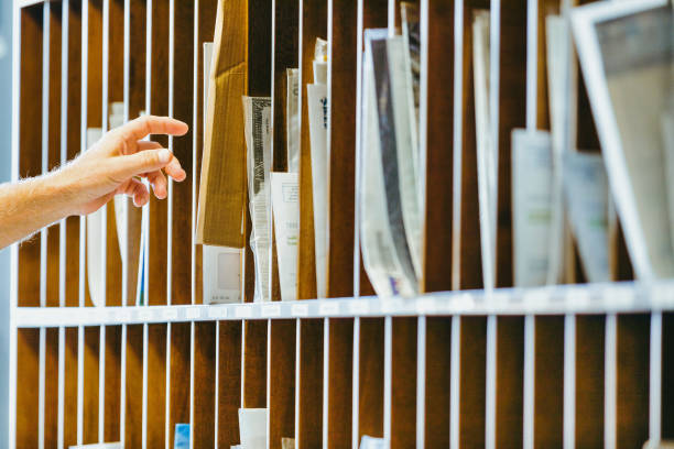 Hand reaches into wooden mail organizer, selecting elderly man's hand reaches into a wooden mail organizer, selecting an envelope from the numerous slots filled with various documents and papers. The scene is well-lit and organized mail sorting room stock pictures, royalty-free photos & images