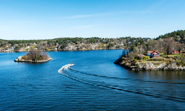 Small Motor boat through in the Stockholm archipelago in Baltic sea with traditional white and red houses at sunny spring evening scenery.
