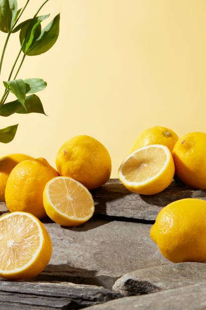 istock Many fresh yellow lemon scattered placed on the rock platform with a green branches on pastel texture. Photo with frontal shot and blank space in center for presentation 2152842708