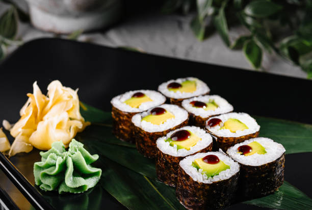 istock Sushi rolls garnished with wasabi and ginger on a modern black plate, botanical backdrop 2152844126