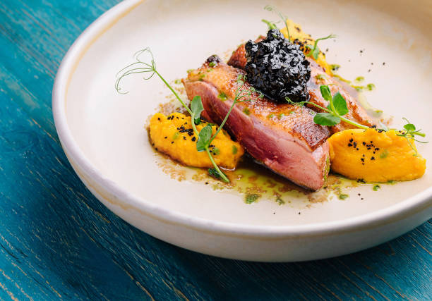 Elegant seared duck breast adorned with caviar and mango puree on a white plate