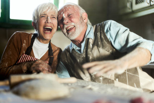 Cheerful mature couple having fun while making a cake in the kitchen.