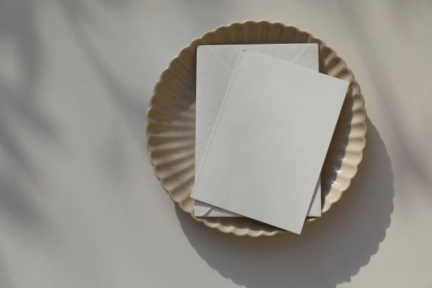 istock Blank greeting card, invitation mockup, envelope in sunlight. Scalloped ceramic plate on beige table background. Soft shadows. Neutral wedding stationery. Food, restaurant, craft concept, flat lay. Top. 2152852789