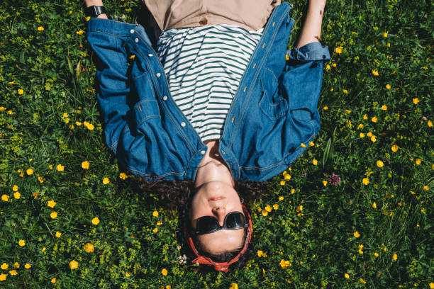 A woman is lying down on the grass surrounded by yellow flowers. Copy space.