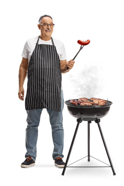 istock Mature man next to a portable barbecue grill holding a sausage with a fork 2152863740