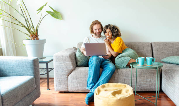 istock Multiracial young couple watching computer laptop sitting on the sofa at home - Happy diverse husband and wife using pc online services - Technology life style concept 2152864373
