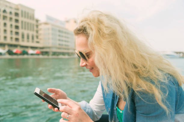 Color image of a young western tourist woman reading good news from her mobile phone while enjoying a day on Dubai Creek.