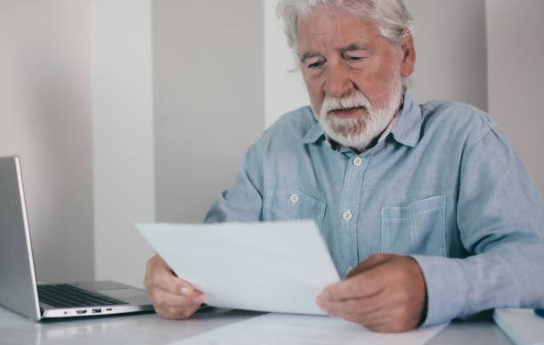 istock Senior bearded financial advisor man consulting documents sitting indoor at home or school classroom holding papers talking with student, client, investor 2152867567