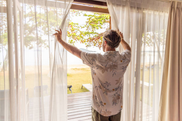 istock Man Opening Curtains to a Beach View 2152868956