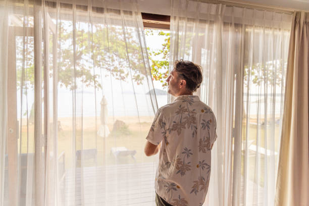 istock Man Looking Out of Window with Sheer Curtains 2152868961