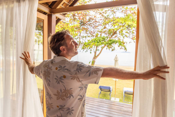 istock Man Opening Curtains to a Beachfront Patio 2152869018