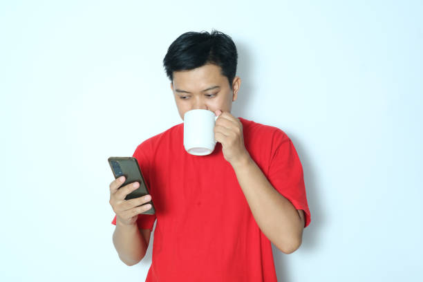 istock Young Asian man is drinking while looking at a smartphone. Wearing a red t-shirt 2152870179