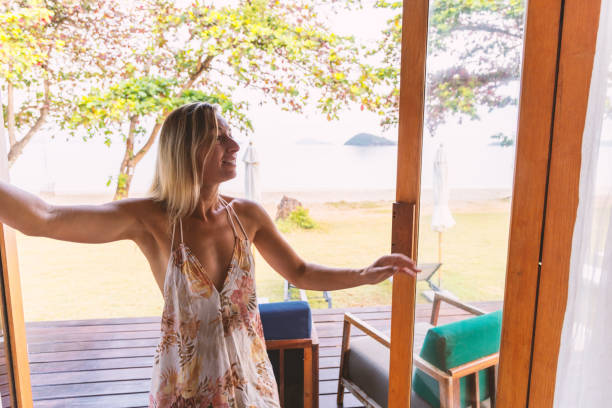 istock Woman Opening Curtains to Beach View 2152873748