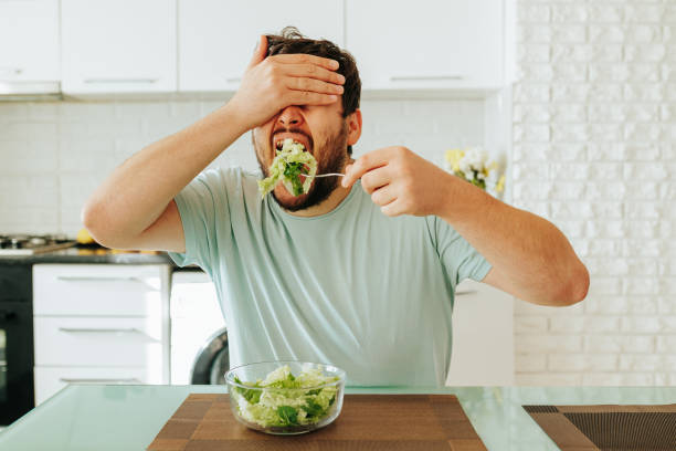 istock Front view, closing his eyes with his hand, the young man brought a fork with salad to his mouth. 2152874578