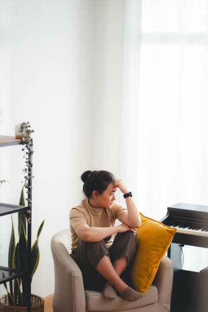 istock Asian woman feeling lonely thinking about problem sitting embracing knees on armchair. 2152878578