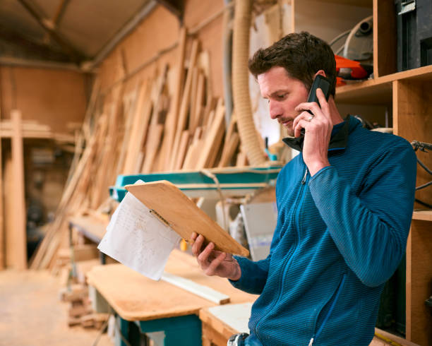 istock Carpenter Working In Woodwork Workshop Making Call On Mobile Phone Whilst Looking At Plan 2152882602