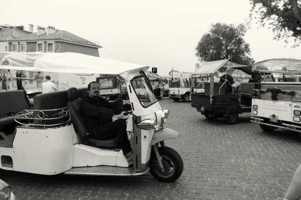 Lisbon, Portugal - Mars 24, 2024: A tuk-tuk driver waits for clients while sitting inside his tuk-tuk on a street in Lisbon downtown.