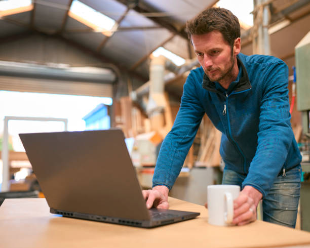 istock Carpenter Working In Woodwork Workshop Using Laptop With Cup Of Coffee 2152883506