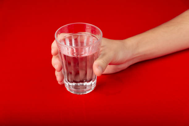 Male hand holding a glass cup with water inside. Isolated on red background.