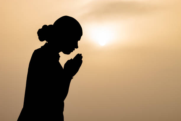 Silhouette of woman praying worship at sunset / sunrise in background/ Religion concept background. Hands in prayer. worship god with religion concept.
