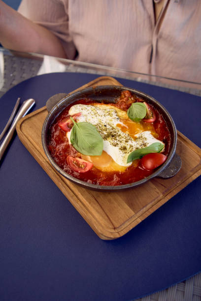 medium sized woman in peach color dress eating Shakshouka in modern restaurant