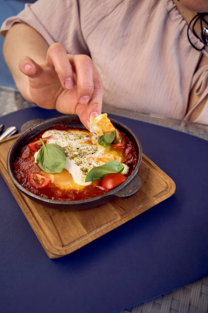 medium sized woman in peach color dress eating Shakshouka in modern restaurant